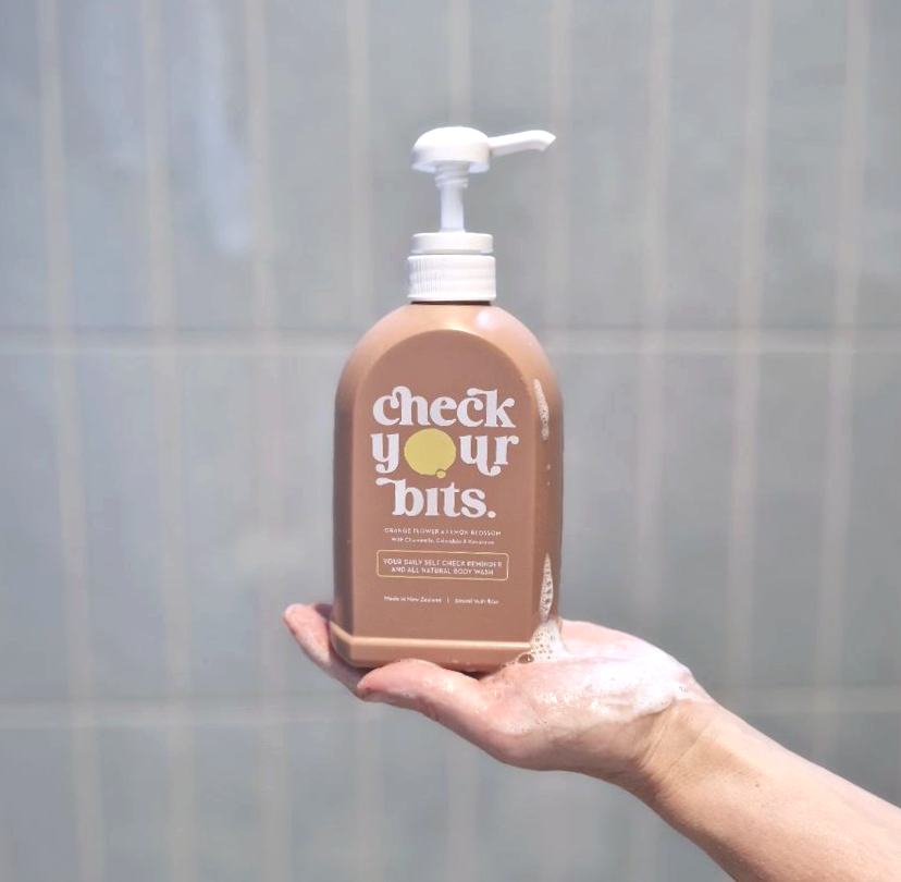 A hand holding the Check Your Bits body wash bottle in the shower